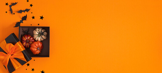 Halloween background banner. Halloween holiday decorations, open gift box with pumpkins and spiders including bats and stars on wide orange colorful background