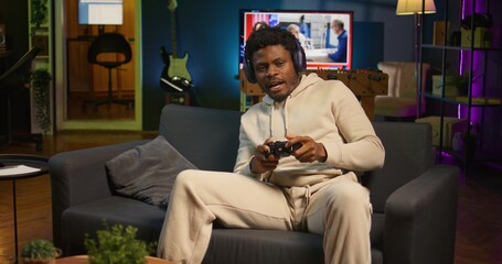 Obraz premium African american man plays intense online video games at home, spamming attack buttons on his controller. Gamer participating in online competition, playing on gaming console. Camera B.
