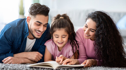 Portrait Of Happy Arabic Family Of Three Reading Book Together At Home, Relaxing On Floor In Living Room, Middle Eastern Mom And Dad Spending Time With Their Kid, Enjoying Domestic Leisure, Closeup