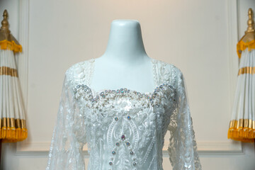 Close-up of an elegant white wedding gown on a mannequin, featuring intricate lace, sequins, and beadwork, set in a ceremonial atmosphere with cultural elements.