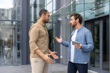 Two men engaged in a heated discussion outside a modern building, possibly a workplace conflict
