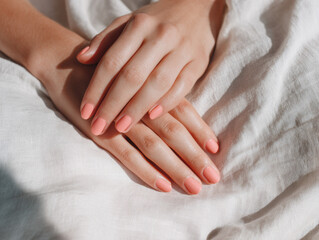 Close-up of hands with a glossy guava-colored manicure resting on soft white fabric, perfect for nail salon promos, beauty campaigns, or skincare and hand care visuals.