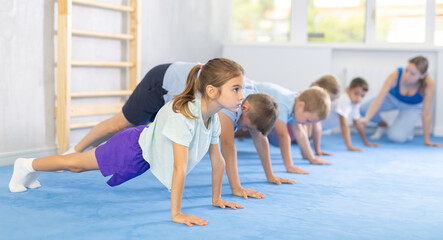 Group of little children doing push-ups on sports mats during a self-defense class in a gym