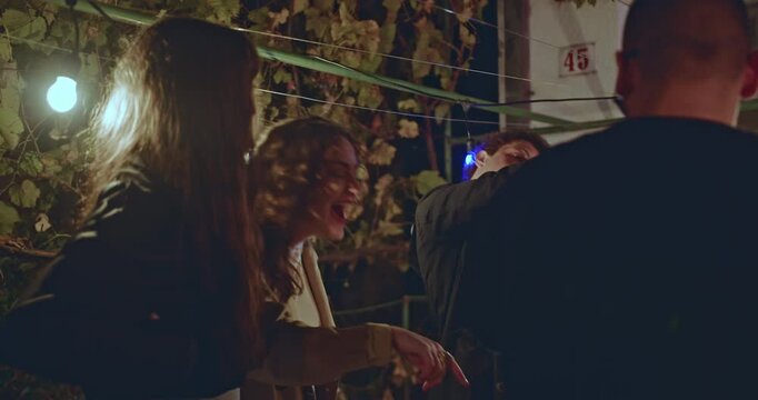 Friends gather in a rustic backyard at night, illuminated by string lights, enjoying conversation and laughter.