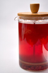 A close-up view of a glass teapot filled with vibrant red liquid, showcasing the steam rising from its surface and a natural wooden lid atop for an inviting presentation.