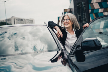 Successful mature businesswoman exiting car in an urban city setting on a bright day with...