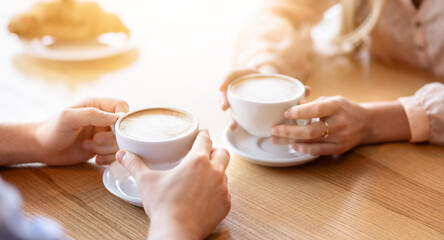 Affectionate young couple on date at cafe, drinking coffee together, cropped view of hands. Unrecognizable guy and his beloved woman enjoying hot beverage, spending time with each other at restaurant