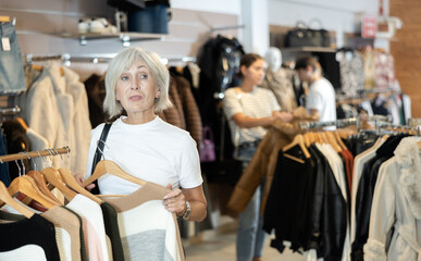 elderly lady carefully examines selection of sweaters, searching for ideal one to keep her warm.