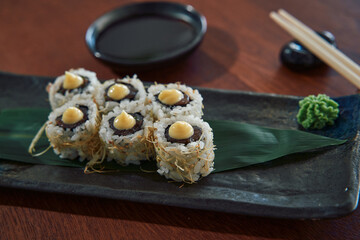 Delicious Sushi Rolls Garnished with Creamy Sauce, Served on a Dark Plate with Wasabi and Soy Sauce for a Flavorful Culinary Experience
