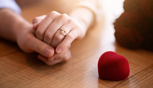 Marriage proposal concept. Young woman wearing engagement ring, holding hands with her husband-to-be at cafe. Millennial couple making decision to get married, closeup view - Powered by Adobe