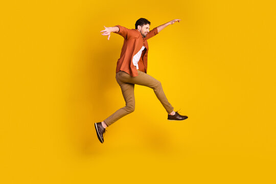 Young man in orange shirt jumping with joy against vibrant yellow background showcasing energy and casual style