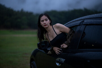 A woman is standing in a car window, looking out at the rain