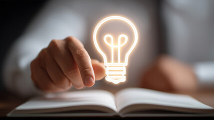 Business hand points to glowing lightbulb rising from open book pages, depicting the spark of insight that turns knowledge into strategic innovation.