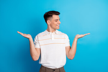 Cheerful young man gesturing and weighing options with confident expression against vibrant blue background