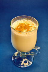 A Creamy Beverage with Spices, Featuring Foam and a Decorative Sprinkle, Served in a Clear Glass Cup Against a Vibrant Blue Background
