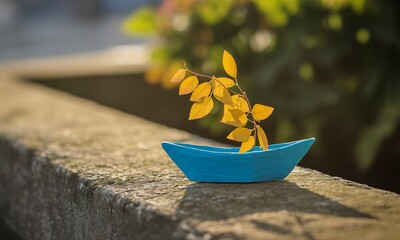 Small blue paper boat with yellow leaf sail on concrete surface outdoors