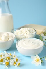 Fresh dairy products and flowers on light blue background, closeup