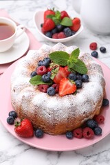 Tasty Bundt cake with powdered sugar and berries on white marble table, closeup