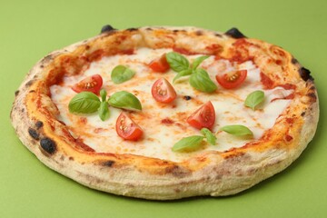 Delicious pizza with tomatoes and basil on green table, closeup