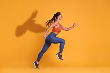 Athletic young woman running against orange background with her shadow in form of hawk. Sports poster