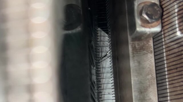 A view into a knitting machine where one of the threads is broken and the knitter is repairing the damage.