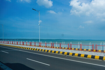 A vibrant photo capturing Suramadu Bridge's road against the Madura Strait and a beautiful, cloudy blue sky