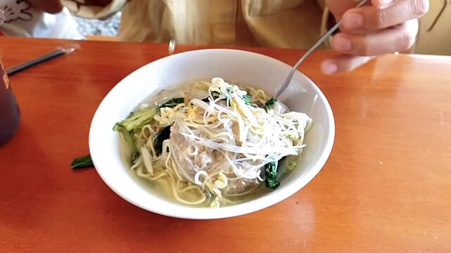 a woman eating Mie Bakso (meatballs with noodle soup) one of the most Indonesia popular street food