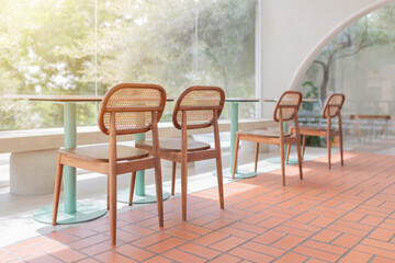 Sunlit modern cafe interior with wooden chairs and green table legs, featuring large glass windows and a warm terracotta tile floor.