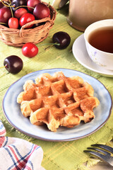 Belgian waffles with cherry and cup of tea on wooden table 