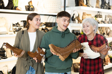 Elderly woman assistant of shoe store helps spouses guy and girl buyer choose right winter boots, comfortable and practical for everyday wear.