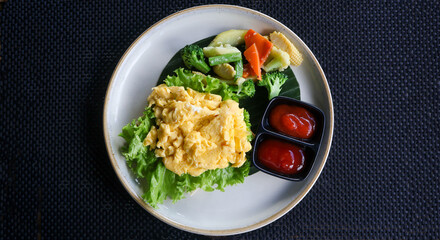 Freshly cooked golden yellow scrambled eggs served hot on a plate with vegetables and condiments. Perfect for breakfast, culinary blogs, food styling, and recipe illustrations. Flat lay, top view.