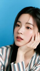 A person with dark hair and striped attire resting their chin on their hand against a blue background