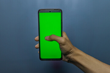 Hand holding smartphone with green screen against blue backdrop