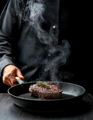 POV of placing a piece of steak on a sizzling cast iron skillet. Smoke rising, juicy texture. Moody lighting with strong contrast. Steam and oil droplets in focus. Black shirt sleeve visible.