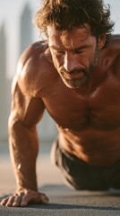 Obraz premium A muscular man performs push ups outdoors, illuminated by warm sunlight. Sweat glistens on his skin. He is shirtless, and his expression is focused and determined.