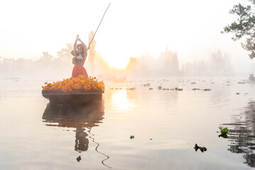 Woman characterized as La Catrina on a trajinera boat with Cempasuchil flowers during sunrise in the canals of Xochimilco, Mexico. 