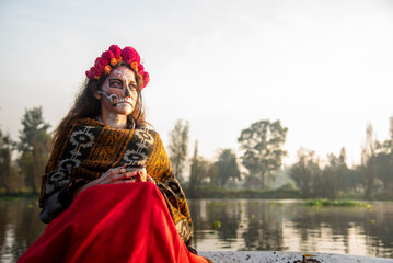 woman characterized as La Catrina on a trajinera boat during sunrise in the canals of Xochimilco, Mexico. 