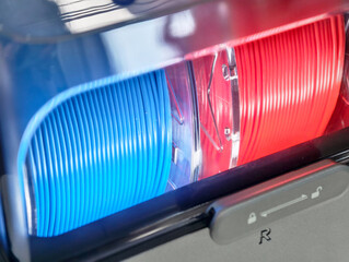 Colorful 3D printer filament rolls in blue and red displayed in a clear storage container