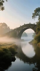 Fototapeta premium Stone Arch Bridge Over a Misty River at Dawn