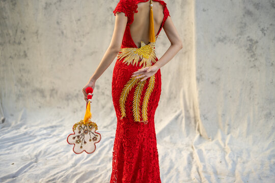 Back view of woman in red lace gown with open back and golden phoenix embroidery, holding ornate decorative fan. Elegant, luxurious, and rich in cultural symbolism.