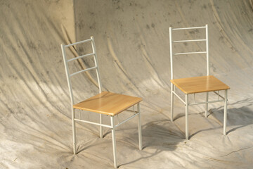 Two simple chairs with light wood seats and white metallic frames placed on a neutral fabric background, conveying minimalism and versatility in furniture design and home decor.