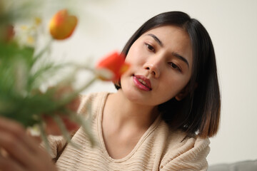 Low angle view shot, Happy young woman is enjoying arranging flowers in a vase in living room at home. Enjoying Weekend.