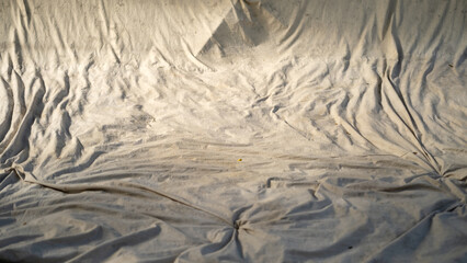 Wrinkled and dirty white fabric spread out under natural sunlight. The textured surface and folds create a raw, rustic backdrop suitable for grunge or abstract design themes.