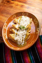 Green enchiladas. Typical Mexican dish made with a folded or rolled corn tortilla filled with shredded chicken and covered with spicy green sauce, cream, grated cheese and onion.