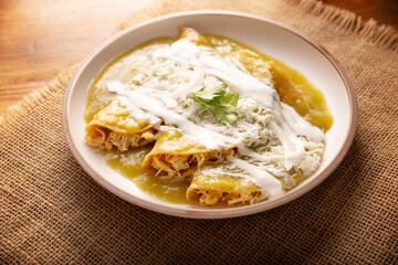 Green enchiladas. Typical Mexican dish made with a folded or rolled corn tortilla filled with shredded chicken and covered with spicy green sauce, cream, grated cheese and onion.