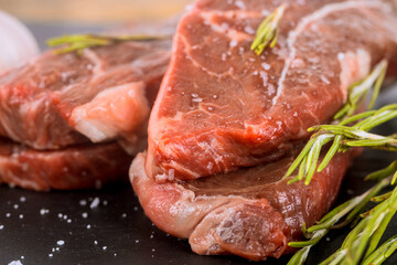 Juicy steaks seasoned with herbs await preparation on wooden kitchen counter.