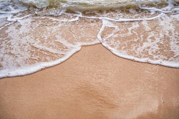 Waves gently lap against a sandy shore during sunset at a tranquil beach location