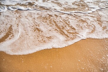 Fototapeta premium Soft waves gently lapping at a sandy beach under the warm sunlight in the afternoon