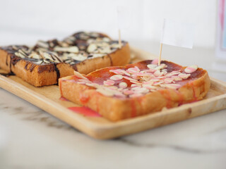 Bread topped with milk strawberries topped with almonds placed in a wooden plate stick white paper flag, snacks, snacks sweet food delicious