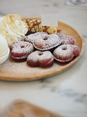 Several red velvet heart-shaped donuts on top icing placed in a wooden plate stick white paper flag, snacks sweet food delicious